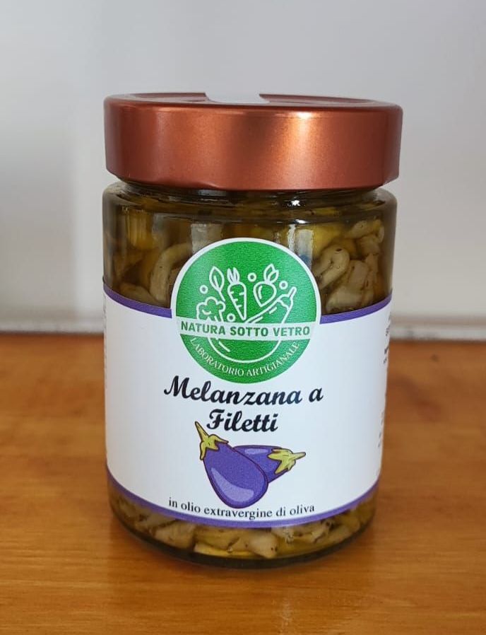 Vasetto di Melanzana a Filetti con etichetta verde e bianca e coperchio in rame su una base di legno.