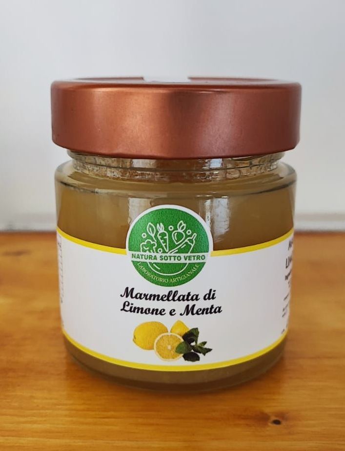 Un vasetto di marmellata di limoni e menta con coperchio in rame ed etichetta bianca, appoggiato su un tavolo di legno.