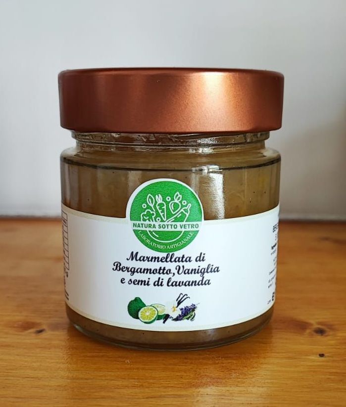 Vasetto di crema spalmabile fatta in casa di melanzane e ricotta con coperchio in rame ed etichetta verde su sfondo bianco.