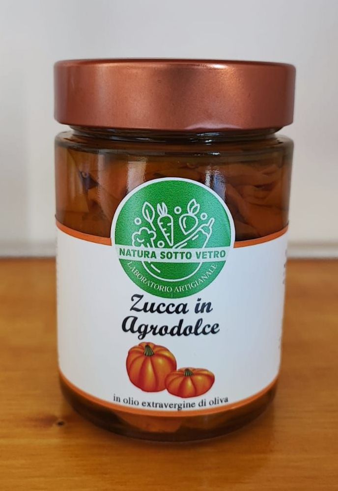Barattolo di vetro con etichetta “Zucca in Agrodolce” e coperchio in rame su superficie bianca.