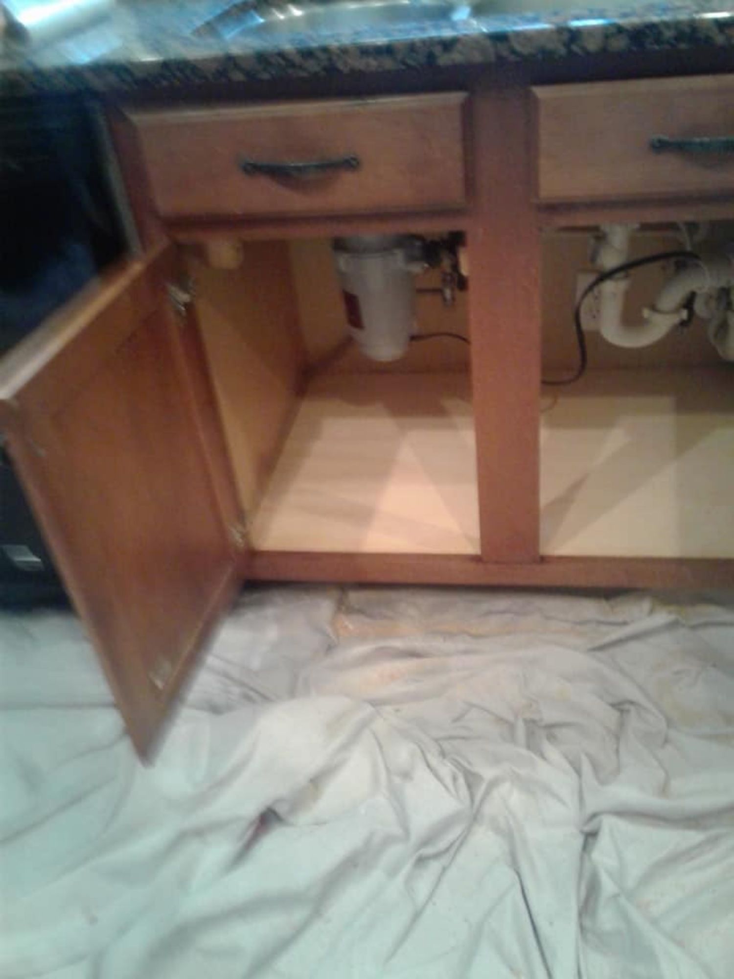 a kitchen sink is under a cabinet with the door open .