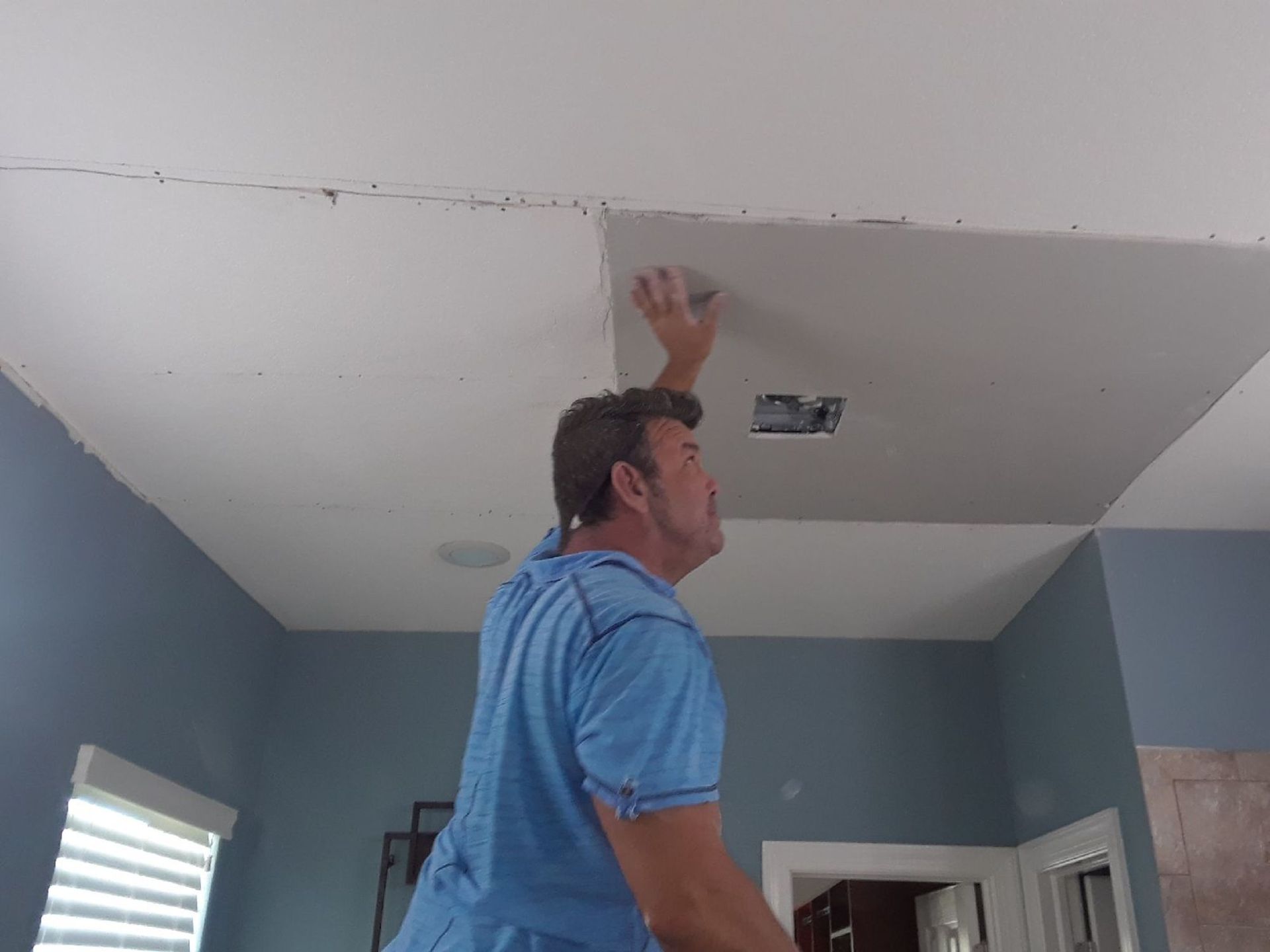 a man in a blue shirt is working on a ceiling in a room .