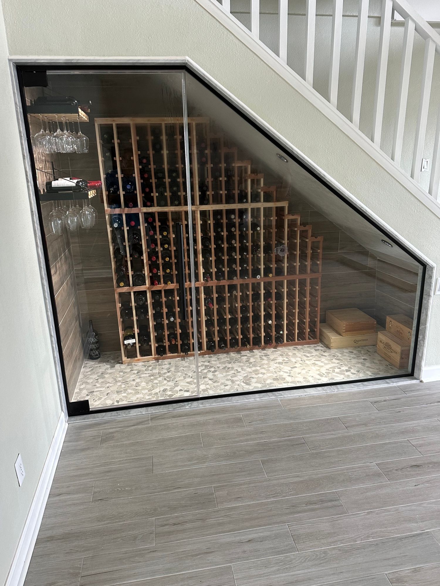 a wine cellar under a staircase with a glass door .