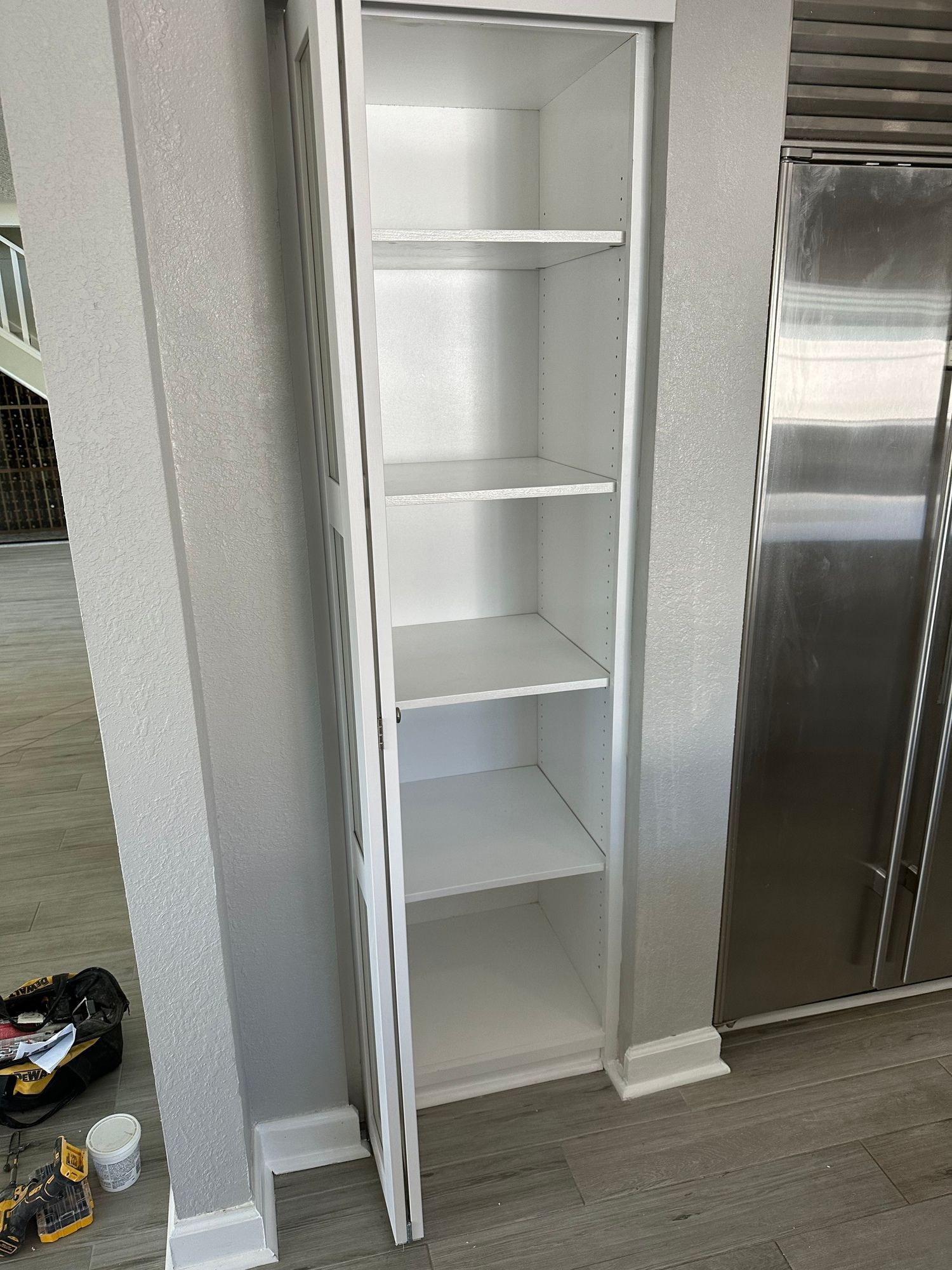 a white shelf in a kitchen next to a stainless steel refrigerator .