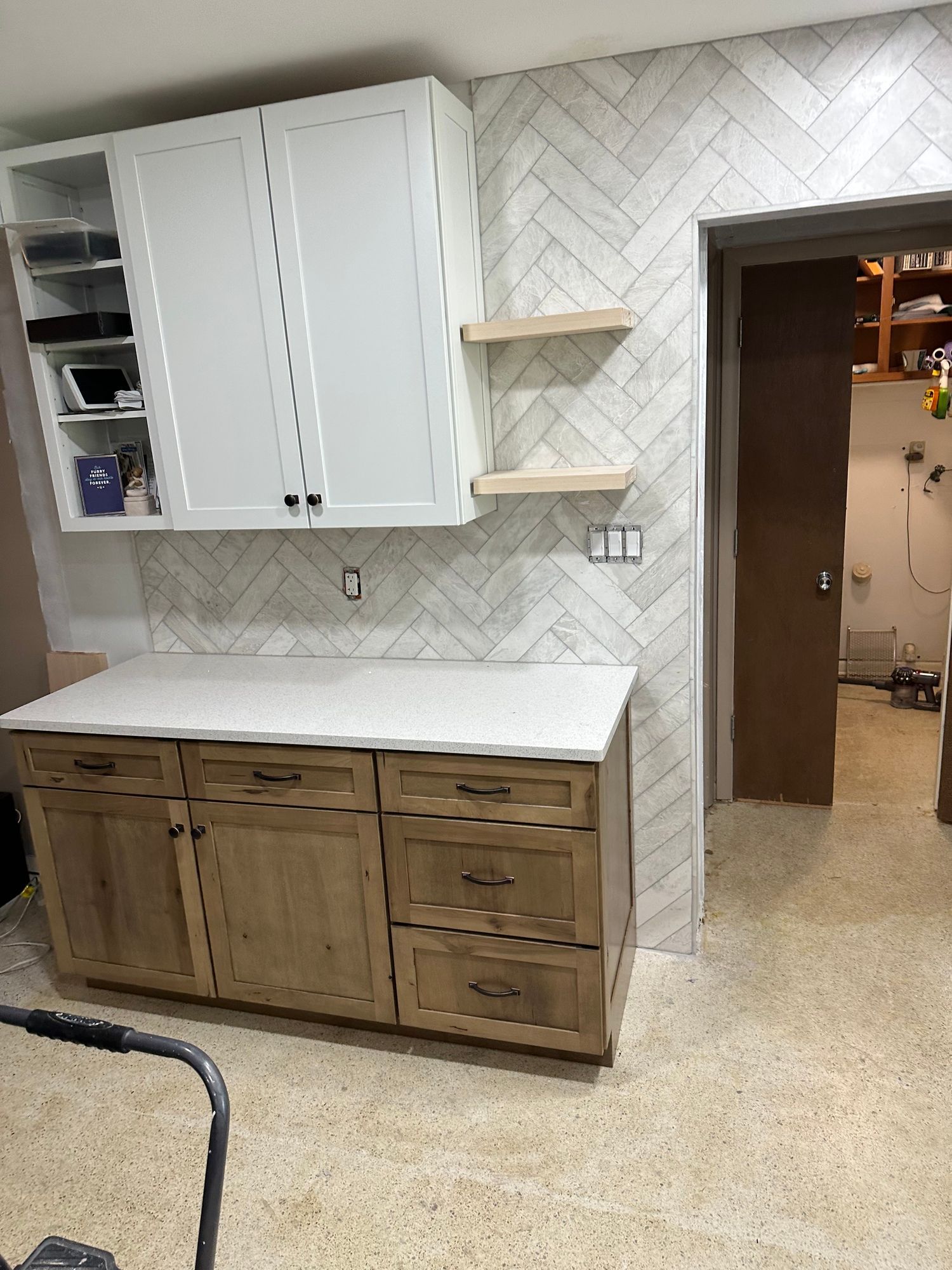 a kitchen with white cabinets and wooden drawers and a herringbone tile wall.