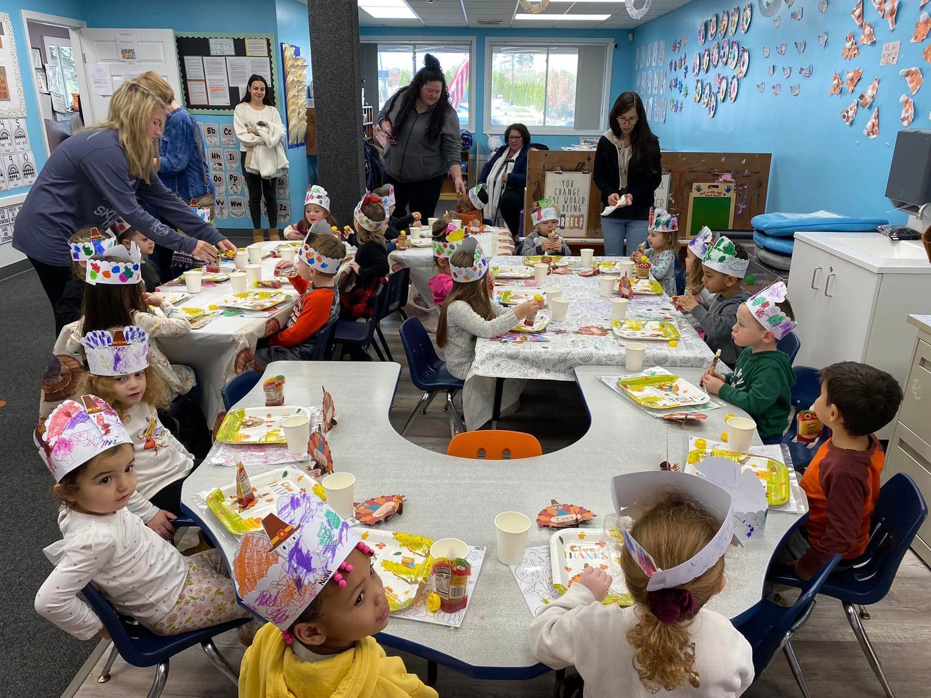 A group of children are sitting at tables in a room wearing paper hats.