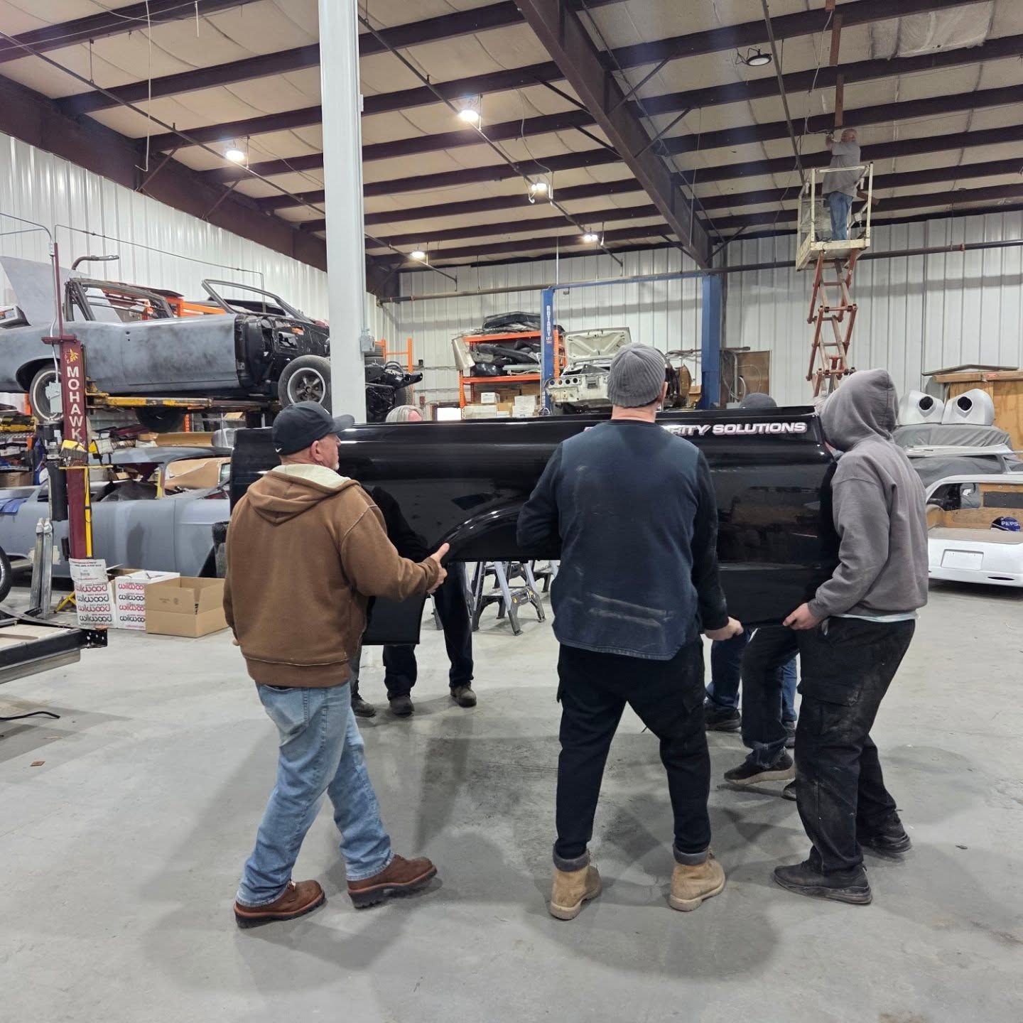 A group of men are carrying a black truck in a garage