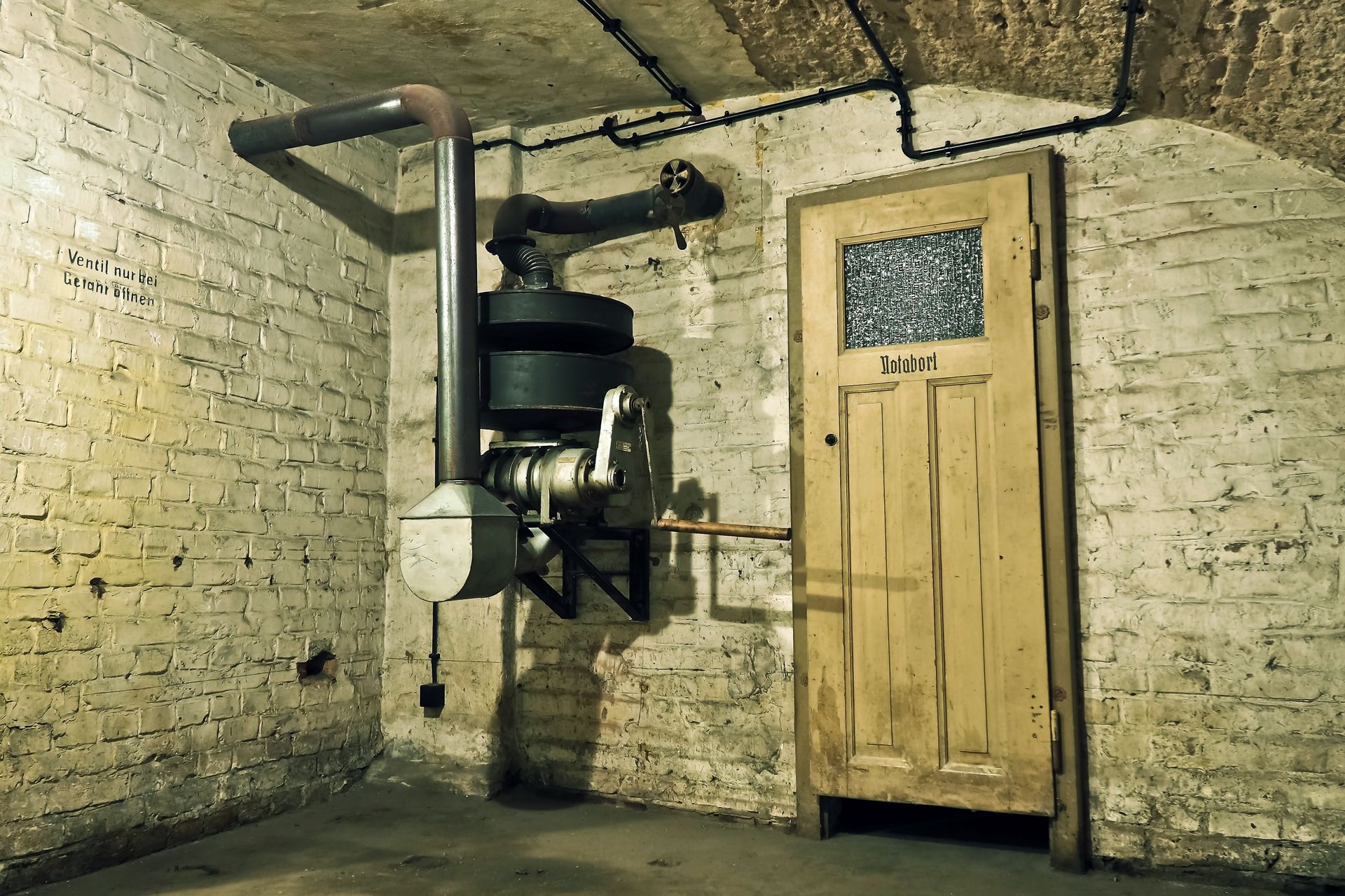 Basement boiler and pipes beside a wooden door in a dim brick room