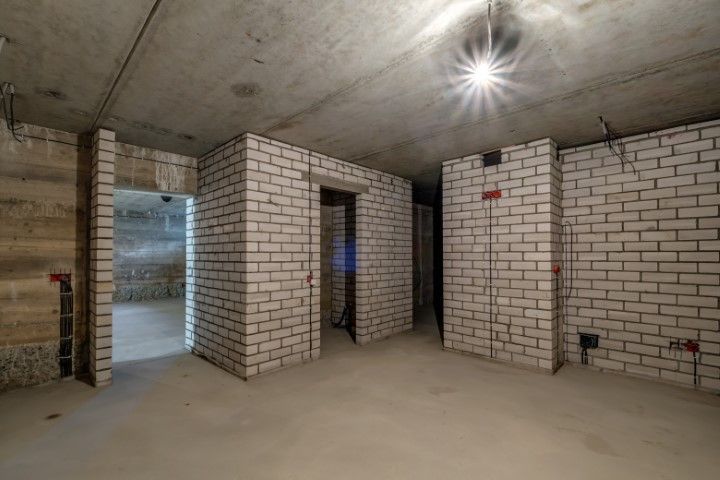 Unfinished basement with white brick walls, concrete floor, and doorway openings under a bare ceiling light