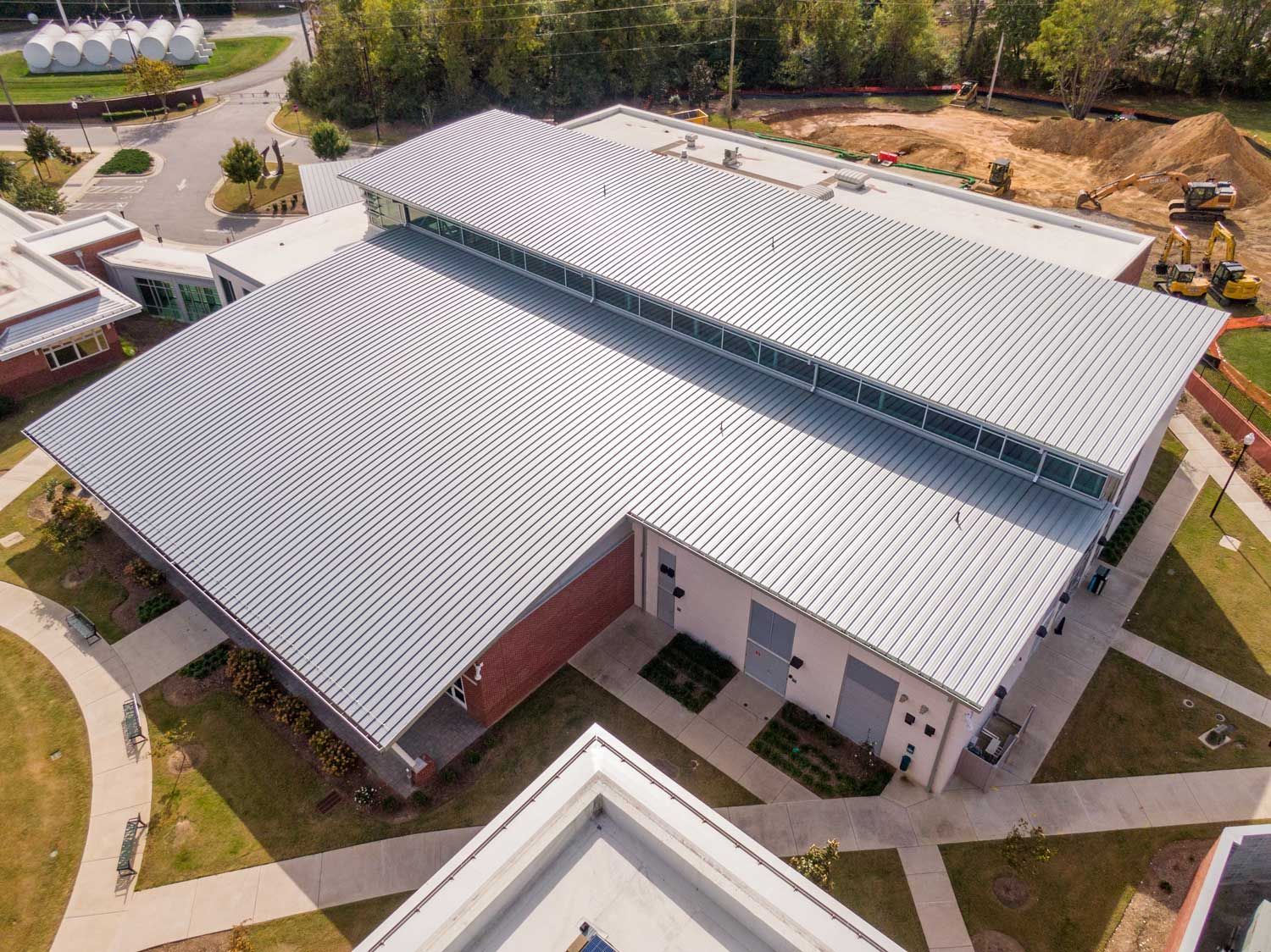 Aerial view of a modern building with a corrugated metal roof. A construction site is visible. Aerial view of a modern building with a corrugated metal roof. A construction site is visible.