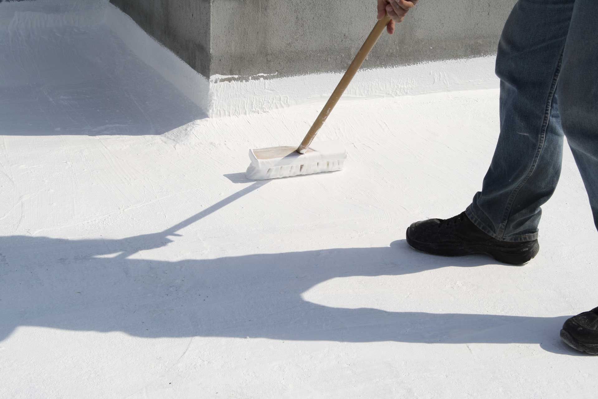 Person applying white coating to a flat roof with a brush. Person applying white coating to a flat roof with a brush.