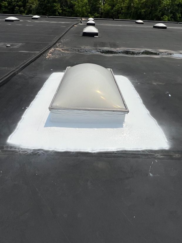 Person using a heat gun and roller to seal a seam on a black flat roof.