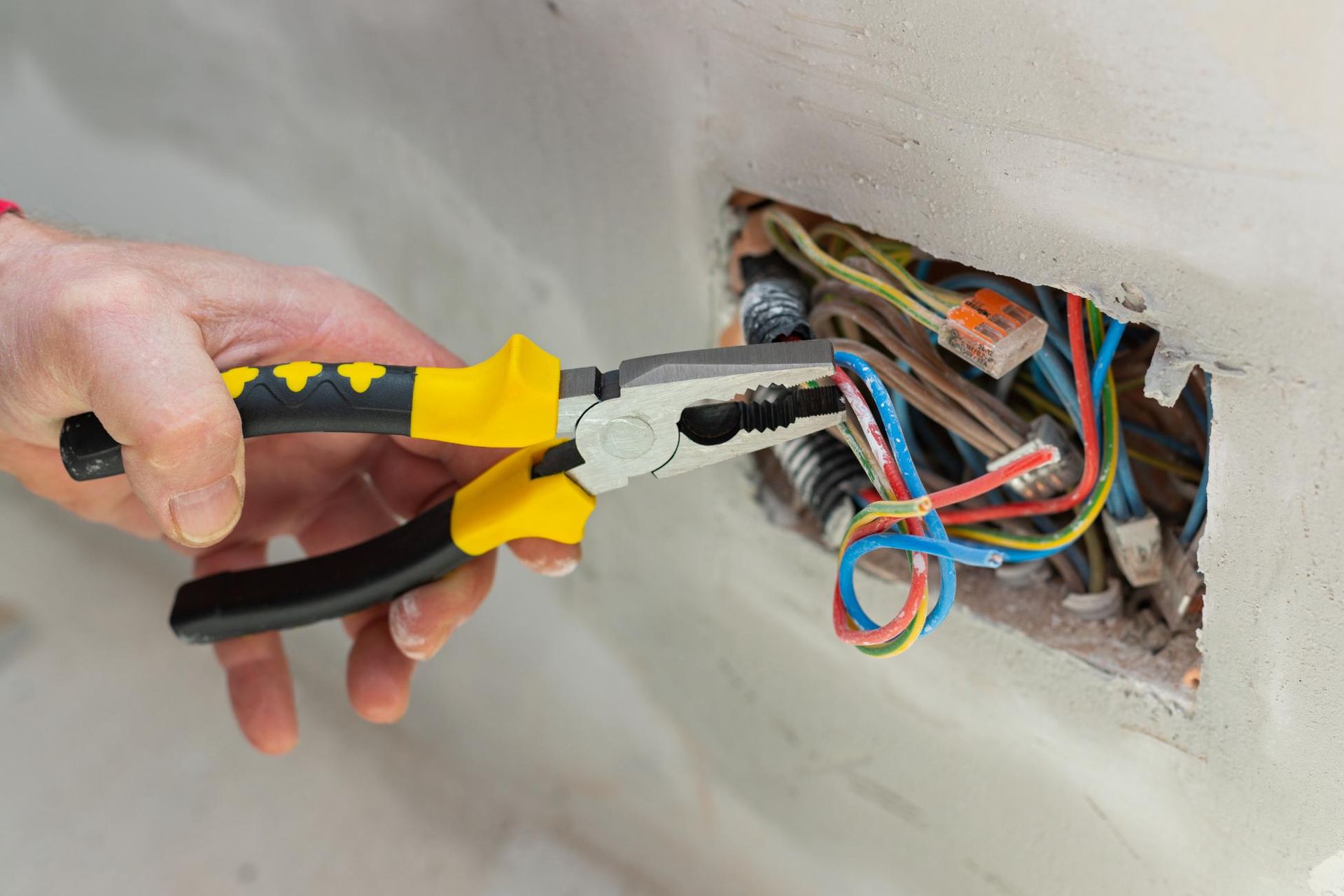 Hand using pliers to work on exposed electrical wiring in a wall.