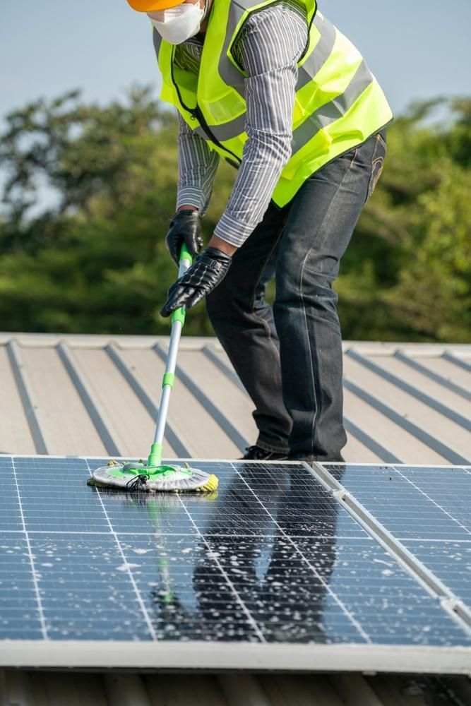 A Man Is Cleaning Solar Panels on A Roof with A Mop — Peter Gow Electrical in Lismore, NSW