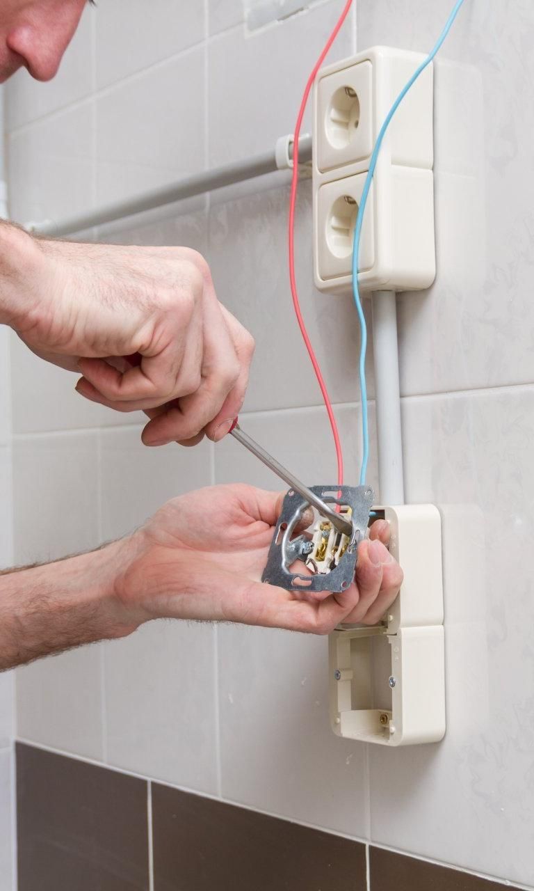 A Man Is Fixing an Electrical Outlet with A Screwdriver — Peter Gow Electrical in Alstonville, NSW