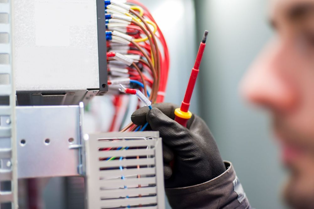 A Man Is Holding a Screwdriver in Front of A Bunch of Wires — Peter Gow Electrical in Lismore, NSW