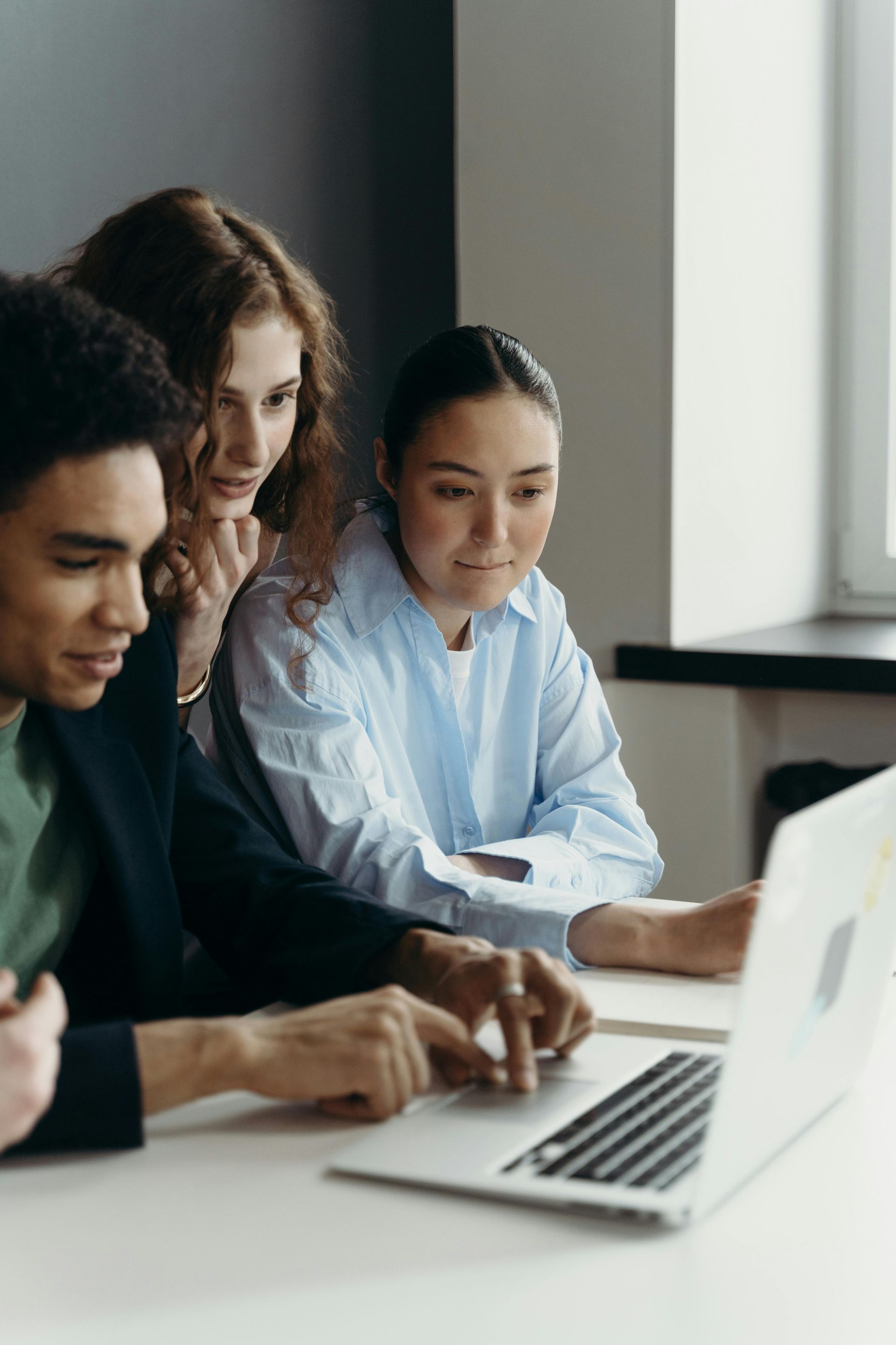 Three coworkers collaborating at a laptop in a bright office