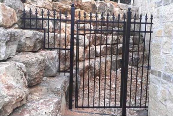 Black wrought-iron gate beside a rocky stone wall and steps outdoors