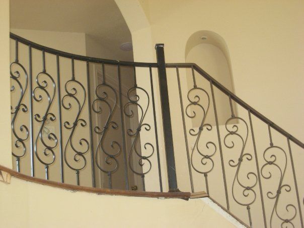 Curved staircase with ornate black iron railing against beige walls