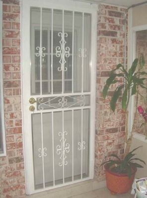 White security door with decorative metal bars beside a potted plant and brick wall.
