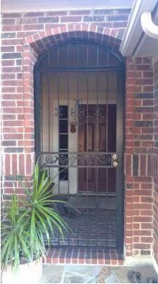 Brick house front door with black security gate and potted plant beside the entrance