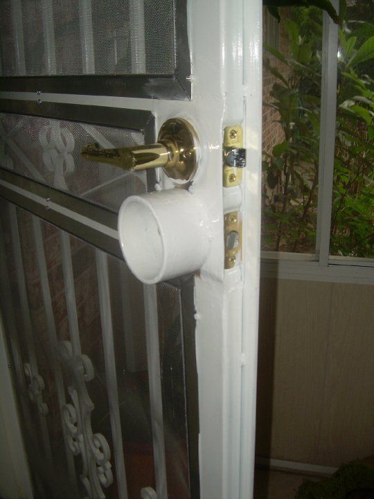 White door with gold handle and a white cylindrical pipe protruding from the lock area, viewed close up.