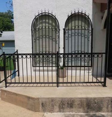 Black wrought-iron railing in front of a white building with two barred arched windows.