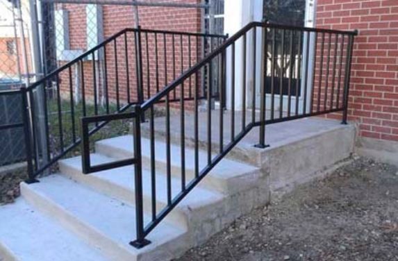 Black metal handrail and concrete steps leading to a brick building entrance