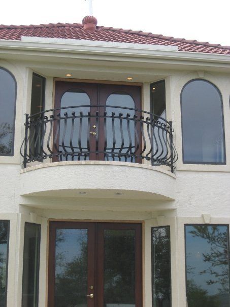 Two-story cream house facade with arched windows, a curved balcony, and a red-tiled roof