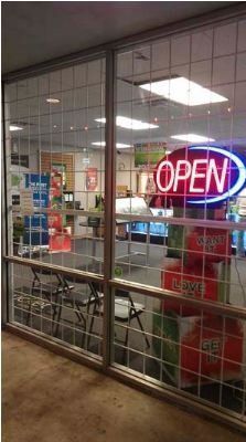 Storefront with neon OPEN sign behind glass, showing shelves and displays inside.