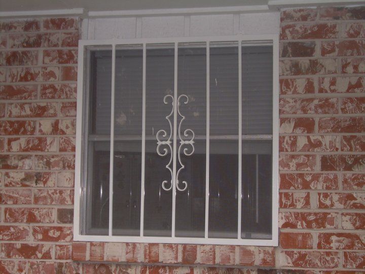 White barred window with a decorative wrought-iron grille in a red brick wall