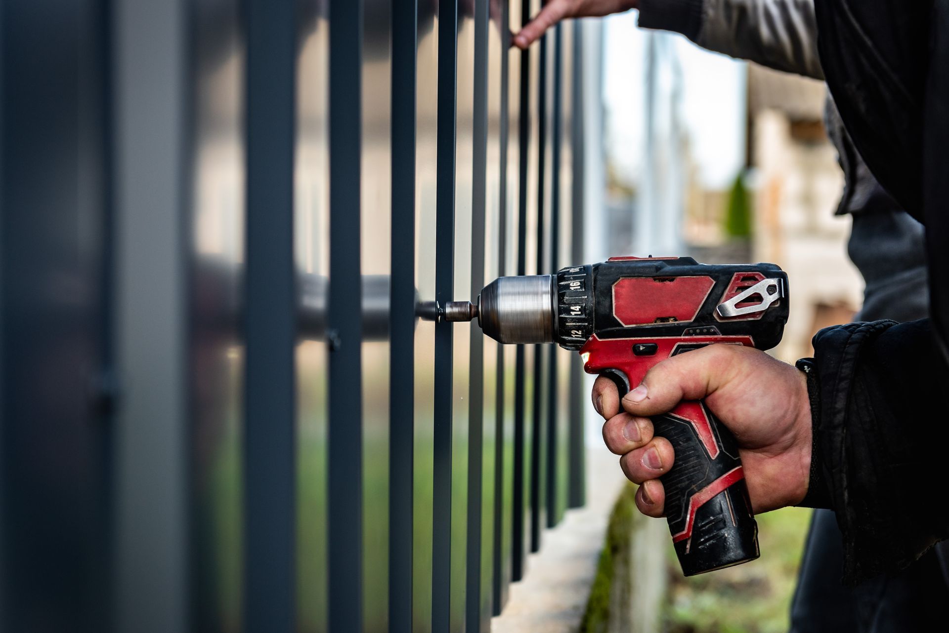 Hand using a red and black drill on a metal fence panel