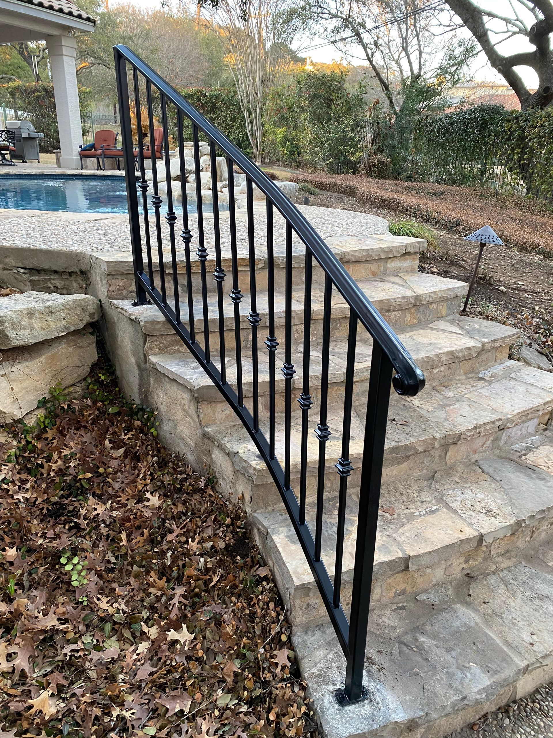 Black metal railing beside stone steps leading to a patio and pool area in a backyard