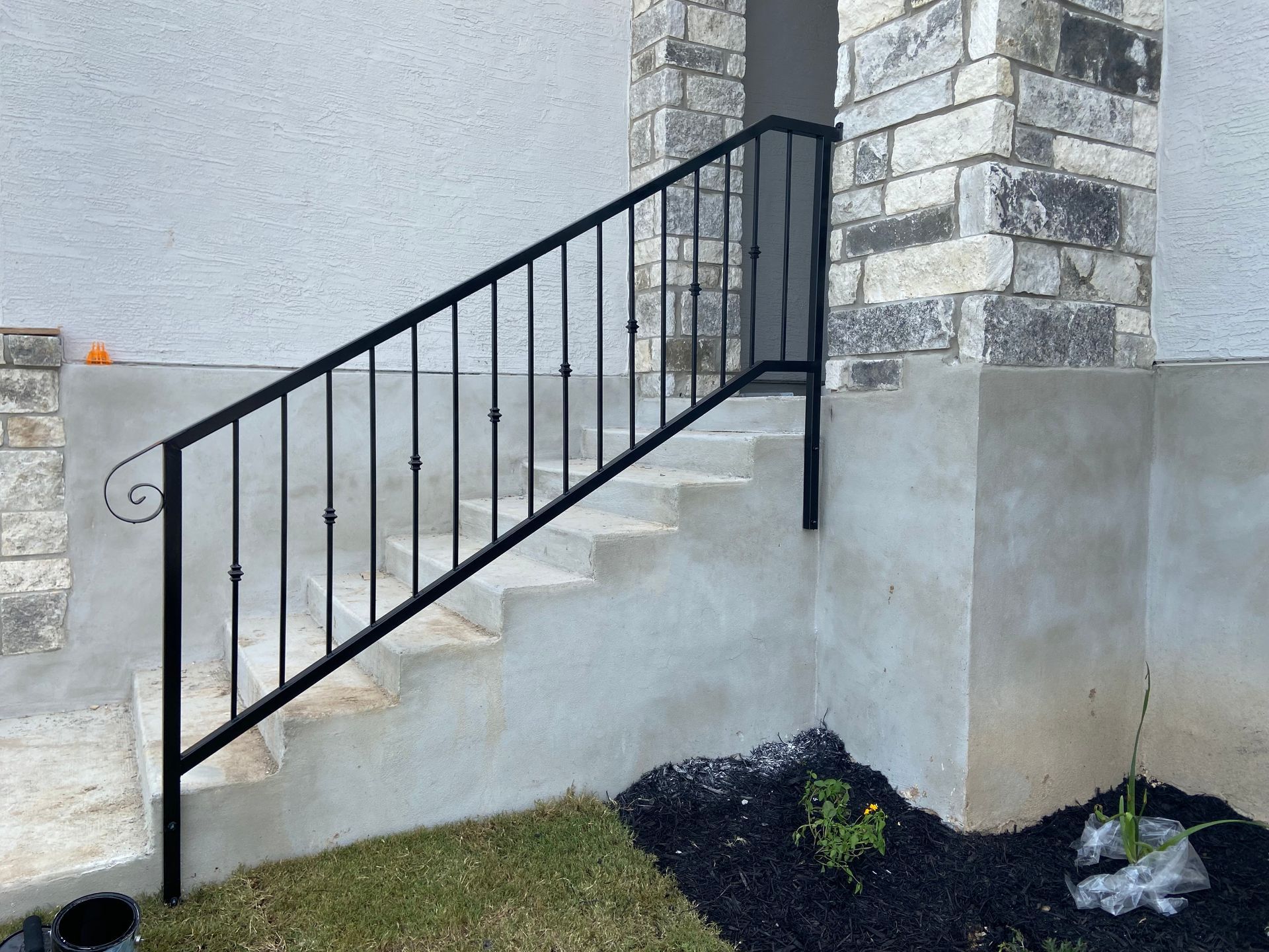 Black metal handrail beside a concrete staircase on a stone house exterior.