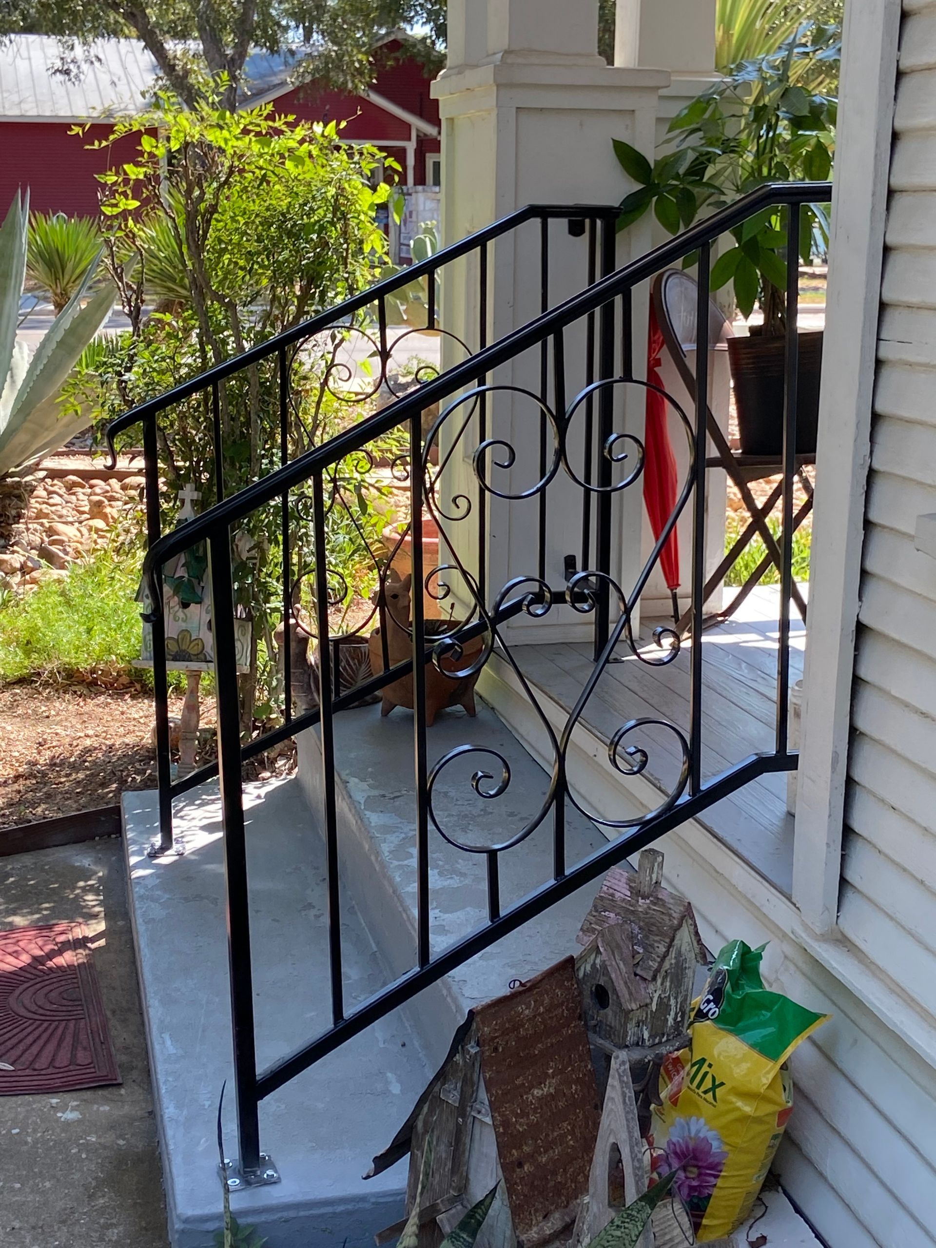 Black iron railing along white front steps with potted plants and garden decor.