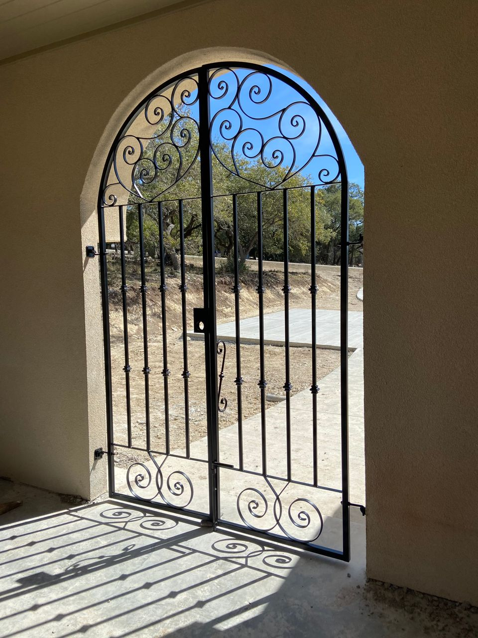 Open wrought-iron gate in an arched doorway, with sunlight casting shadows onto the floor.