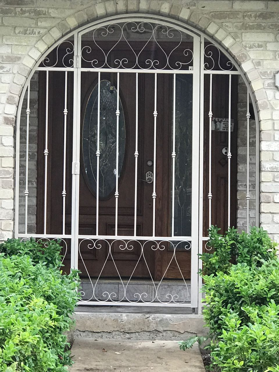 White metal security gate in front of a stone-arch doorway with plants on either side