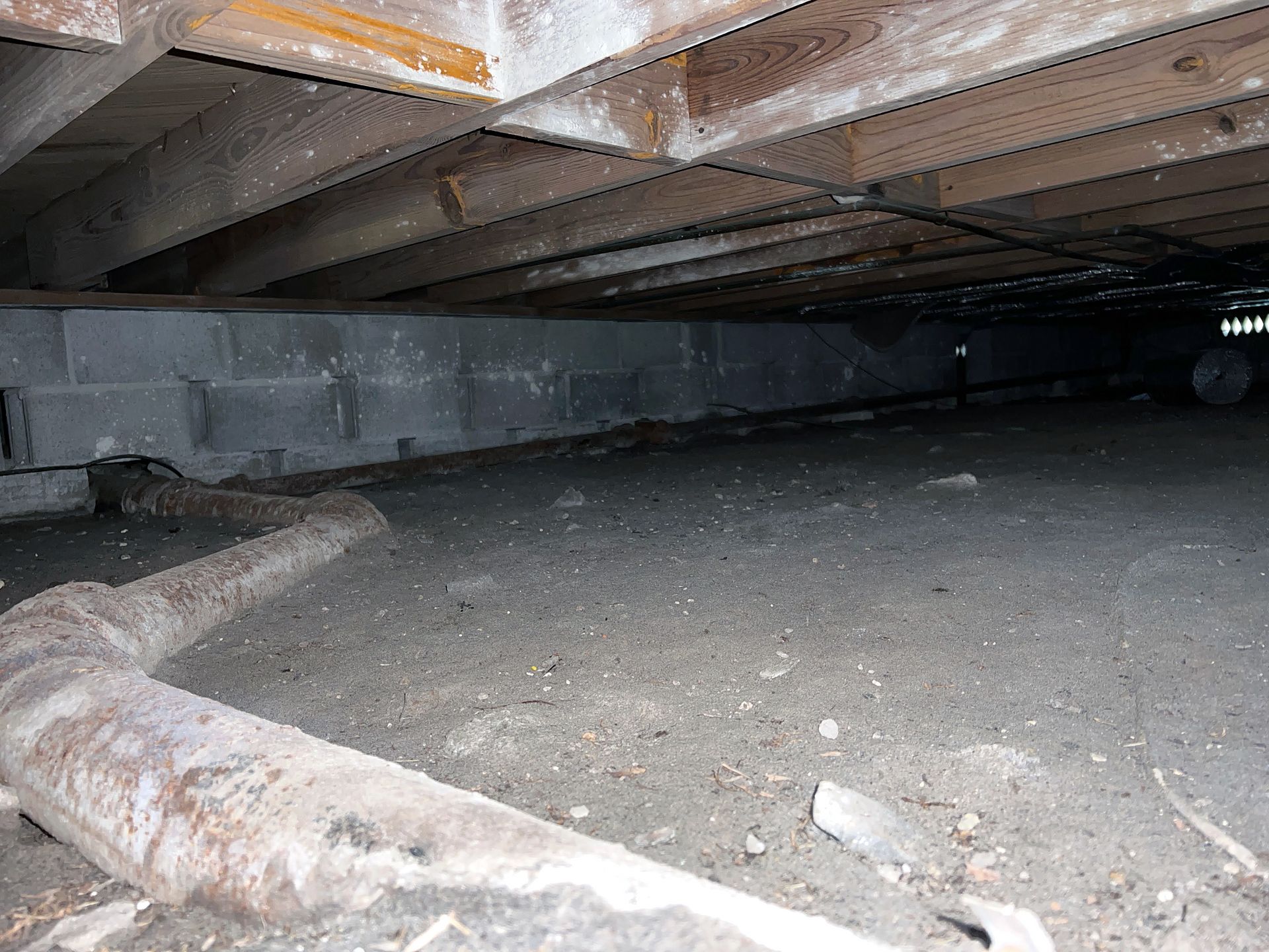 A worker kneels on a concrete floor inside a crawlspace enclosed with plastic sheeting, measuring the space with a tape. A worker kneels on a concrete floor inside a crawlspace enclosed with plastic sheeting, measuring the space with a tape.