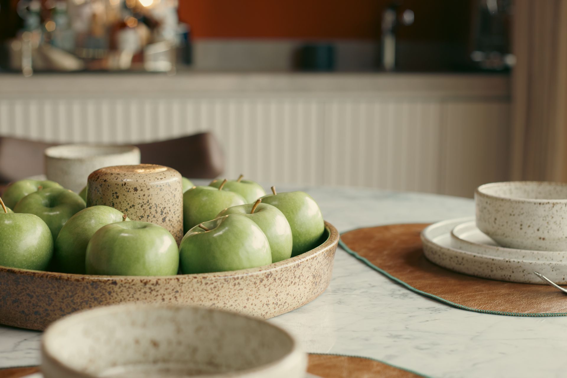 Uma tigela de maçãs verdes está sobre uma mesa ao lado de pratos e tigelas.