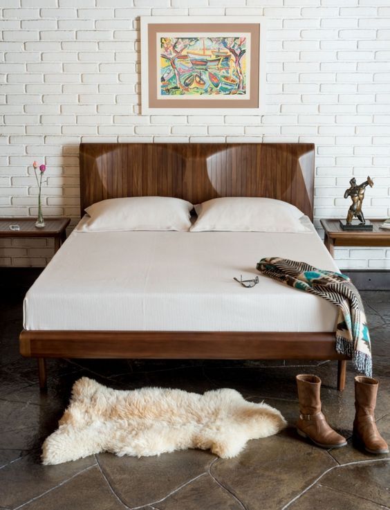 Um quarto com cama, tapete, botas e um quadro na parede.