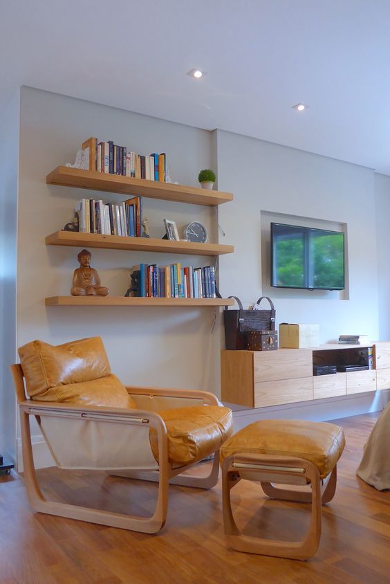 Uma sala de estar com cadeira, pufe, estantes e televisão.