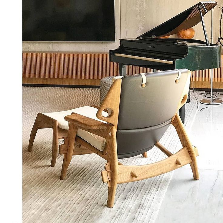 Uma cadeira e um pufe estão em uma sala de estar ao lado de um piano.