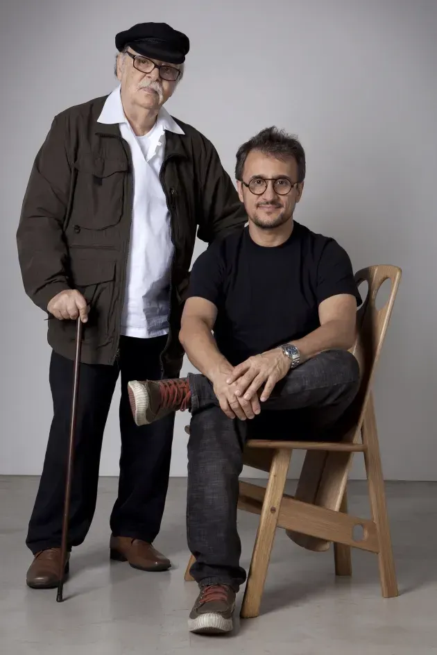 Um homem com uma bengala está parado ao lado de um homem sentado em uma cadeira.