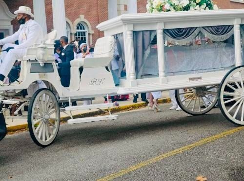 White horse-drawn carriage with a canopy and white flowers on a street during a parade