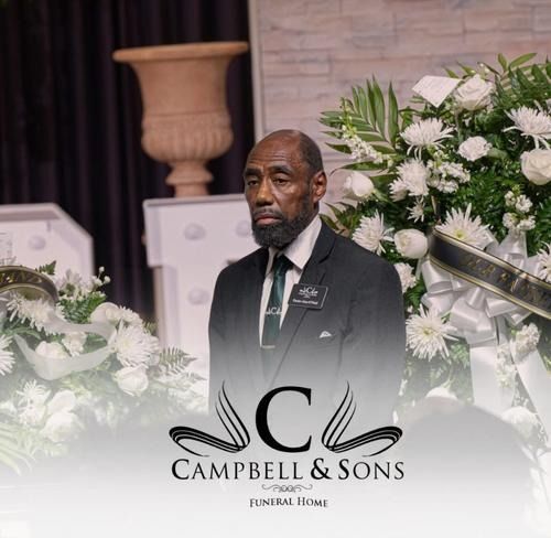 Man in a black suit standing among white floral arrangements at Campbell & Sons Funeral Home