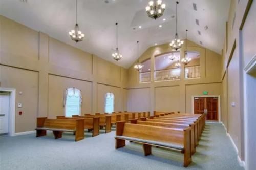 Empty church sanctuary with wooden pews, hanging lights, and a high arched ceiling