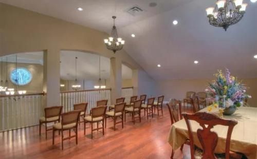 Spacious banquet hall with rows of wooden chairs, chandeliers, and a floral centerpiece on a table