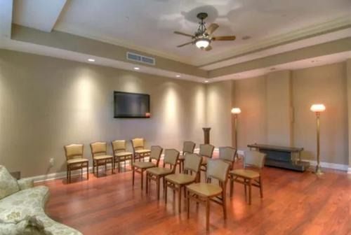 Empty meeting room with rows of chairs, wall-mounted TV, floor lamps, and wood flooring