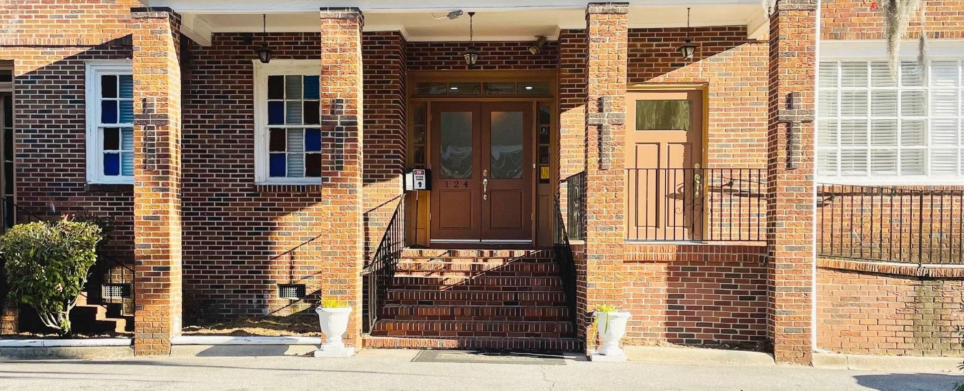 Brick building entrance with wooden double doors, steps, columns, and windows on either side