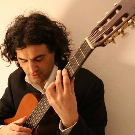 Uomo che insegna a qualcuno a suonare la chitarra acustica, in casa.